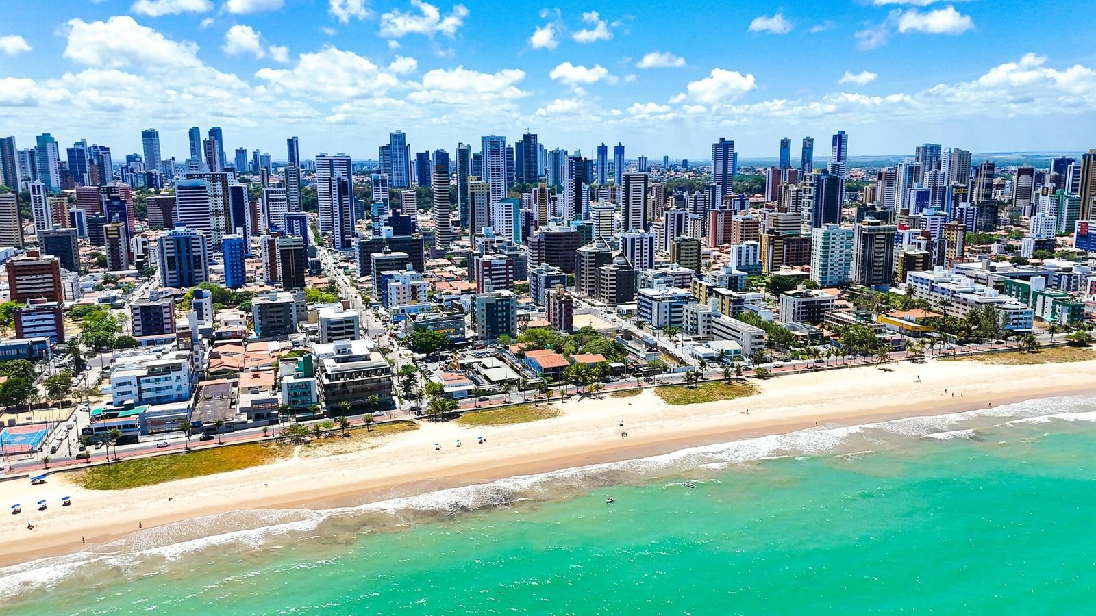 Vista aérea da orla de Manaíra, em João Pessoa: prédios, coqueiros, faixa de areia e mar verde-azulado