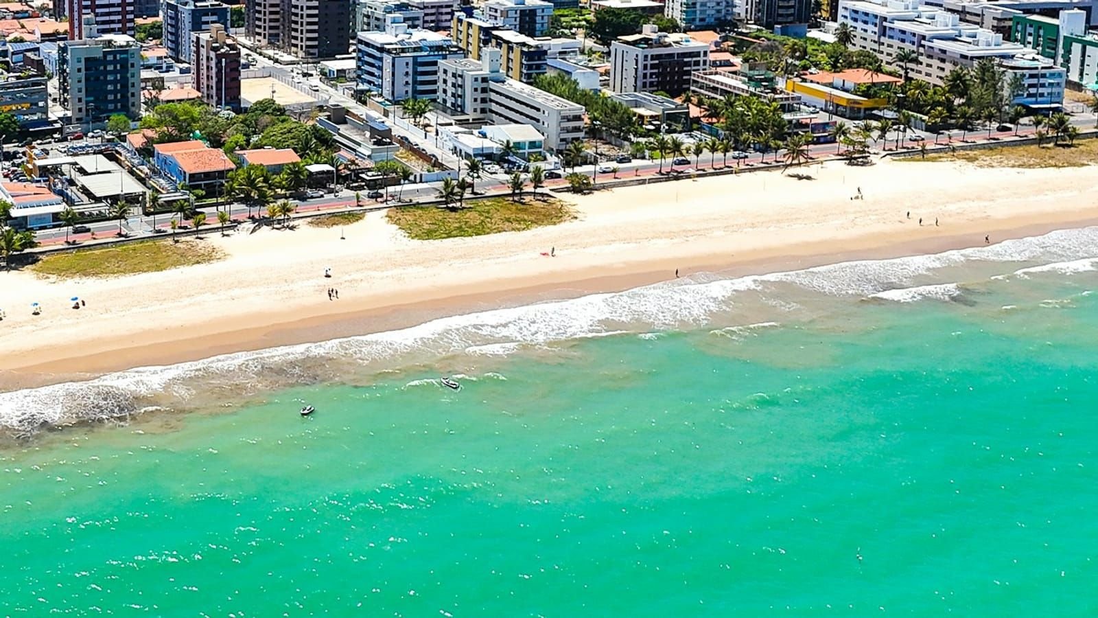 Vista aérea da orla de Manaíra, com calçadão, ciclovia, coqueiros, areia e mar verde-azulado