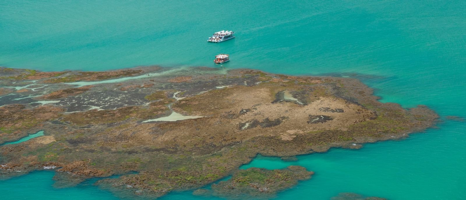 Vista aérea das piscinas naturais de Picãozinho, com recifes e barcos em água turquesa